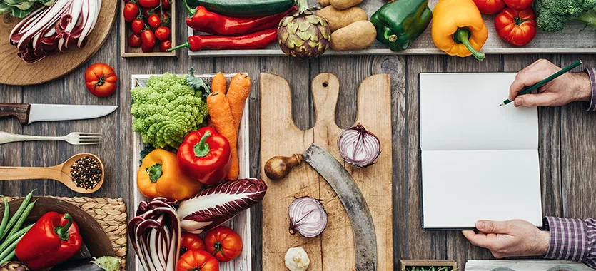 Vegetables and a blank notebook on a kitchen table